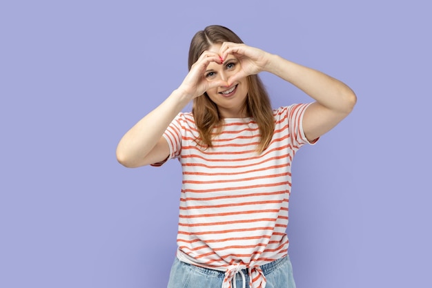 Mujer haciendo forma de corazón con las manos delante de sus ojos expresando amor amistad cuidado