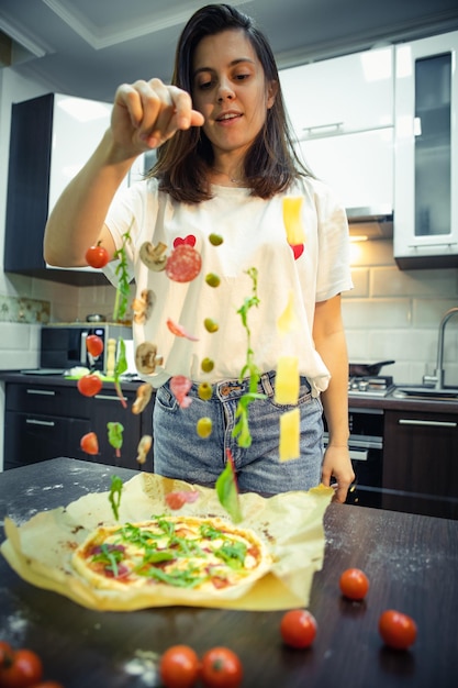 Mujer haciendo ingredientes de pizza como salami champiñones queso de oliva congelado en el aire