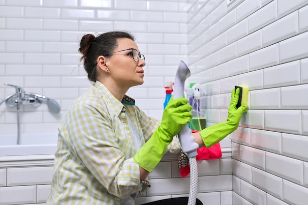 Mujer haciendo limpieza de baño en casa, pared de azulejos de lavado femenino con vapor. Usar un limpiador a vapor para una limpieza rápida