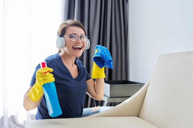 Mujer haciendo limpieza de casa mujer en auriculares y guantes con detergente