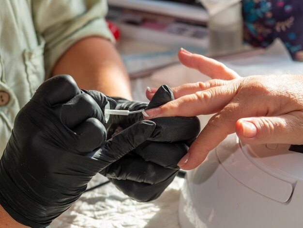 Mujer haciendo manicura aplicando esmalte francés para pintura de uñas permanente