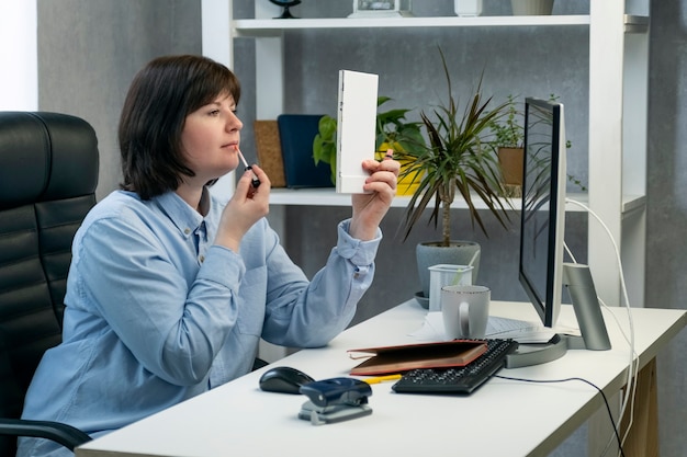 Mujer haciendo maquillaje y acicalarse en el lugar de trabajo. Chica pinta sus labios en el trabajo en la oficina privada.