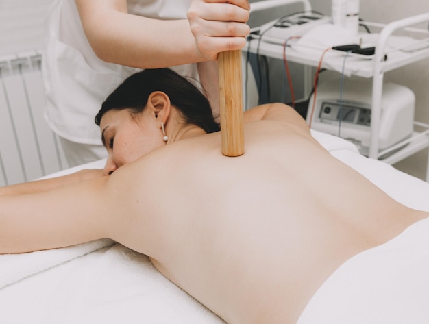 Mujer haciendo masaje de espalda con palo de bambú en el centro de spa wellness