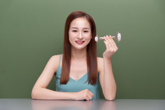 Mujer haciendo masaje con rodillo de jade rosa. Herramientas de belleza para tratamientos faciales.