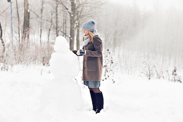 Mujer haciendo un muñeco de nieve en invierno