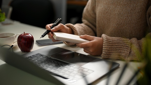 Una mujer haciendo notas en su bloc de notas en espiral tomando una lista de importancia en papel en su escritorio