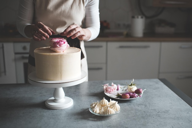 Foto mujer haciendo pastel decorando con rosas de flores permaneciendo en la mesa de la cocina cerca de casa