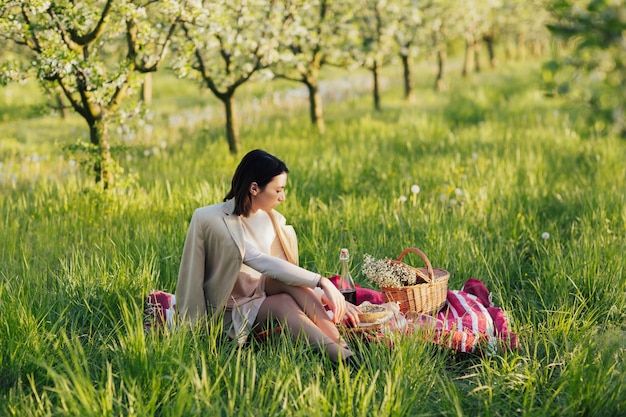 mujer haciendo un picnic en el soleado día de primavera en el huerto durante la temporada de flor de manzana