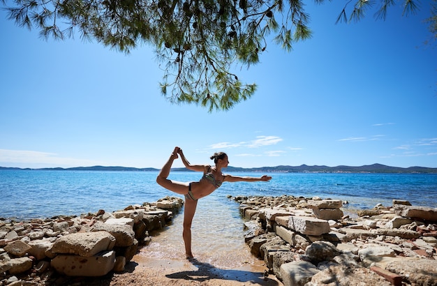 mujer haciendo pose de yoga cerca del agua de mar
