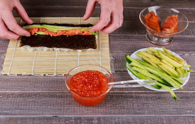 Mujer haciendo rollos de sushi japonés en casa de cerca