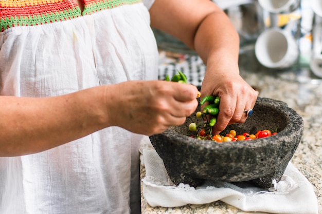 Mujer haciendo salsa mexicana en un molcajete de piedra con tomates y chiles