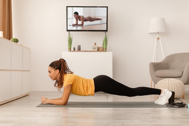 Mujer haciendo tablón viendo canal deportivo en tv en casa