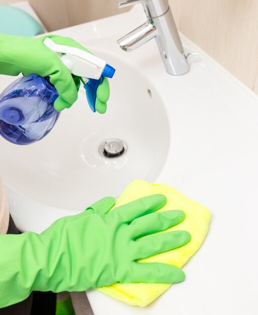 Mujer haciendo tareas domésticas en el baño, limpiando el fregadero y el grifo con spray.