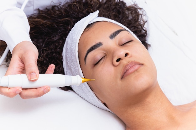 Mujer haciendo tratamiento facial con chorro de plasma en clínica de belleza.