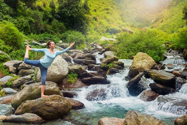 Mujer haciendo yoga asana Natarajasana al aire libre en cascada