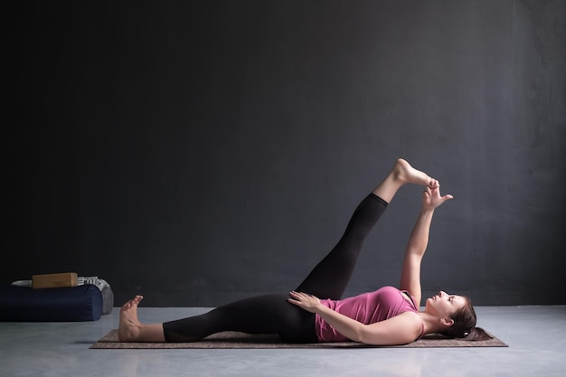 Mujer haciendo Yoga asana Supta padangusthasana o mano reclinada a la pose del dedo gordo del pie