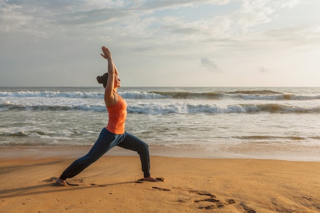 Mujer haciendo yoga asana Virabhadrasana 1 Guerrero Pose en la playa en