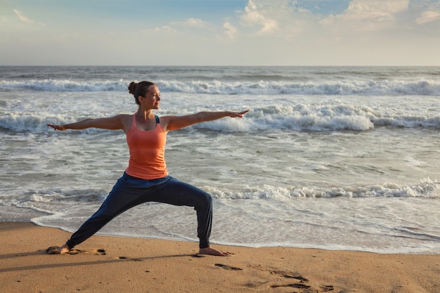 Mujer haciendo yoga asana Virabhadrasana 1 Guerrero Pose en la playa en