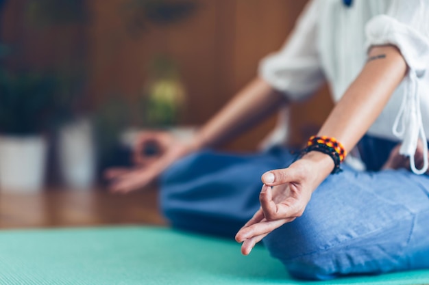 Mujer haciendo yoga en casa sentada en postura de loto con los dedos en posición mudra