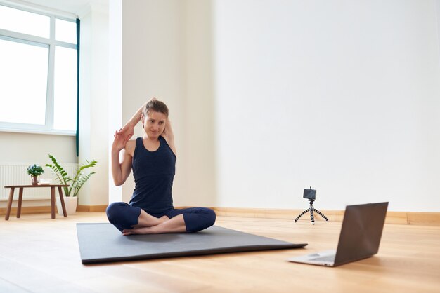 Mujer haciendo yoga en línea. Computadora y cámara en su sala de estar. Estilo de vida saludable y conceptos de trabajo a distancia.