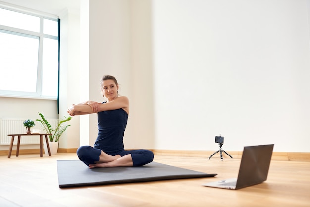 Mujer haciendo yoga en línea. Computadora y cámara en su sala de estar. Estilo de vida saludable y conceptos de trabajo a distancia.