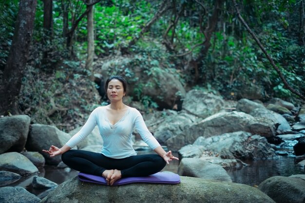 Mujer haciendo yoga meditación pose al aire libre en el arroyo tropical en el bosque