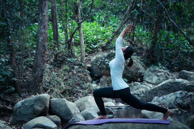 Mujer haciendo yoga meditación pose al aire libre en el arroyo tropical en el bosque