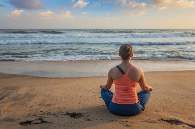 Mujer haciendo yoga en la playa - Padmasana lotus pose