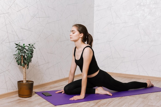 mujer haciendo yoga en pose de media paloma y practicando la atención plena mientras se sienta en la alfombra