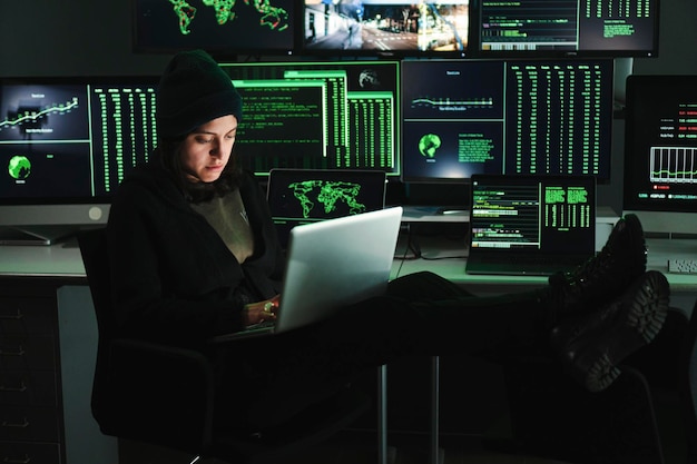 Mujer hacker informática escribiendo código en la computadora portátil en el fondo muchas pantallas de computadora con datos Joven programadora haciendo un ataque de firewall o phishing con el concepto de seguridad cibernética en línea