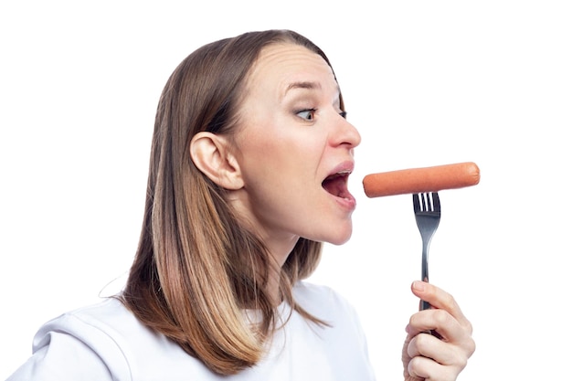 Una mujer hambrienta con la boca abierta come una salchicha de un tenedor Deliciosa comida chatarra rápida Aislada sobre fondo blanco Primer plano