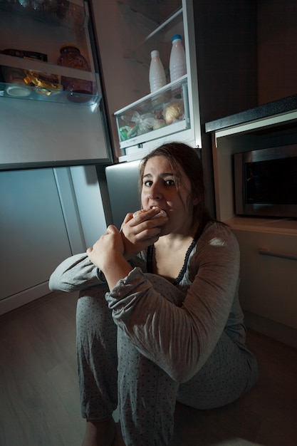 Mujer hambrienta comiendo en el piso en la cocina en la noche