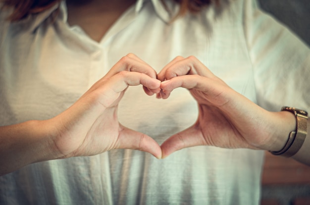 Mujer hecha a mano en forma de corazones y en el pecho con amor, mano en forma de corazón de amor.