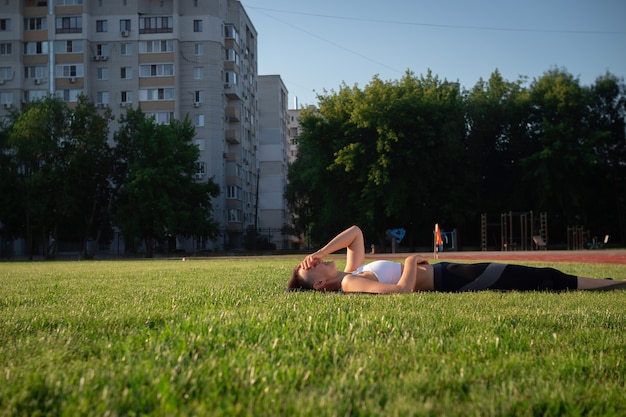 Una mujer hermosa, alegre y alegre está tumbada en el césped del parque y sonriendo.