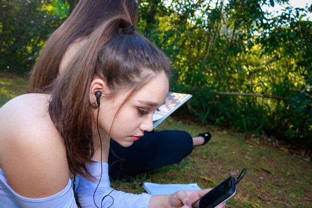 Una mujer hermosa con un amigo usando el teléfono mientras se relaja en el parque