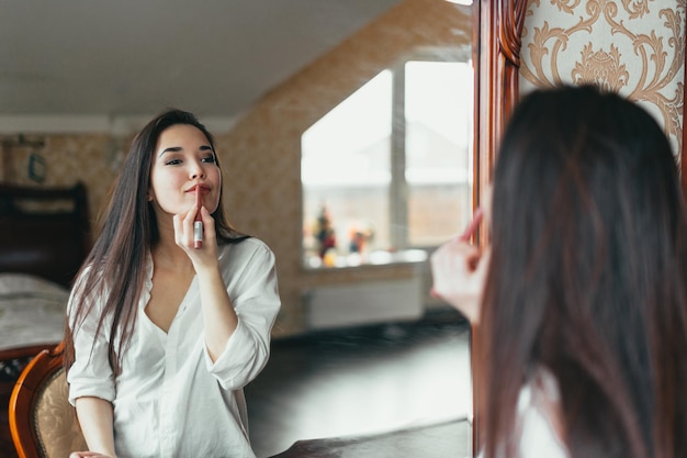 Mujer hermosa aplicando lápiz labial frente al espejo en casa