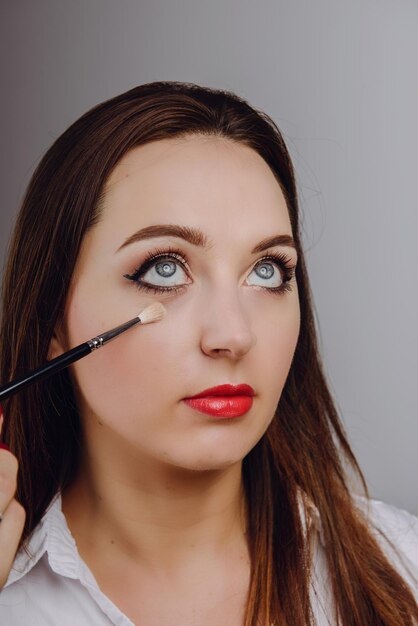 Mujer hermosa aplicando maquillaje contra un fondo gris