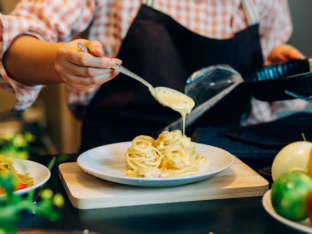 La mujer hermosa asiática durante hace la comida de los espaguetis en la cocina