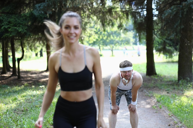 Mujer hermosa atleta y hombre cansado detrás en el parque en jog