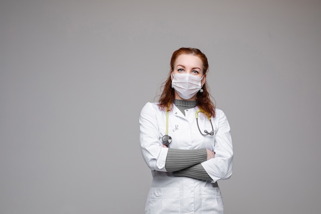 Mujer hermosa en bata médica blanca, máscara y fonendoscopio sobre sus hombros