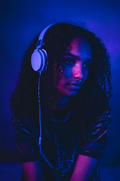 Mujer hermosa con cabello rizado escuchando música a través de auriculares en el cuarto oscuro