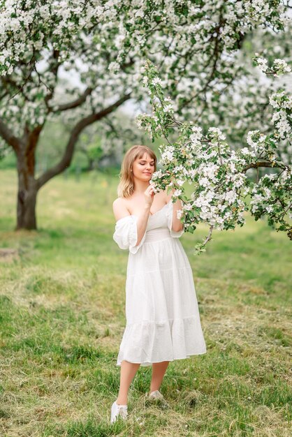 Foto una mujer hermosa camina en el jardín de primavera una chica con un vestido blanco en los manzanos en flor.