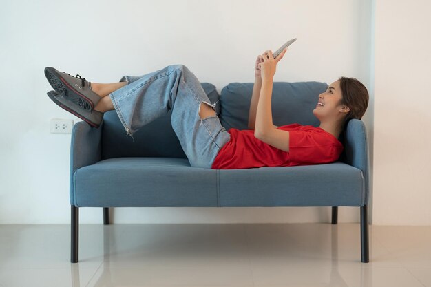 Una mujer hermosa con una camisa roja está acostada en el sofá jugando con una tableta