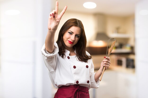 Mujer hermosa chef haciendo gesto de victoria sobre fondo desenfocado