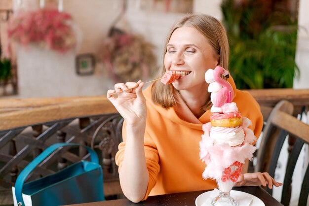 Mujer hermosa come postre en forma de flamenco rosado en la cafetería tiempo para la diversión votos en una sudadera brillante