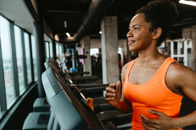 Mujer hermosa y dedicada con el cabello afro atado corriendo en una cinta de correr en el gimnasio