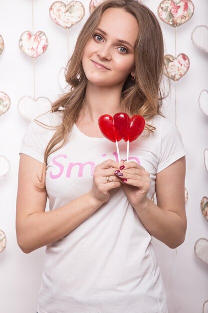 Mujer hermosa divertida que sostiene el caramelo en forma de corazón