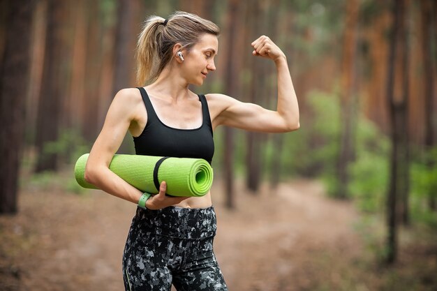 Mujer hermosa con una estera de yoga al aire libre.