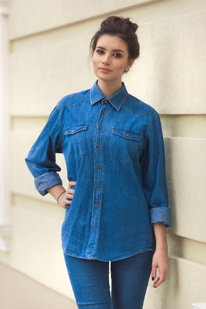 Mujer hermosa con estilo en camisa de mezclilla de pie cerca de la moda de estilo wall Street denim total