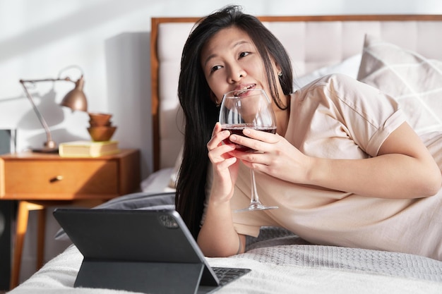 Mujer hermosa feliz con ropa informal hablando por videollamada en una tableta digital acostada en la cama